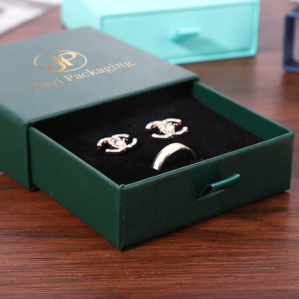 Open green jewelry drawer box with a black velvet interior, ring and earrings